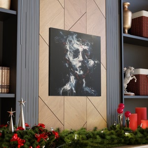 May include: Square canvas art featuring an abstract portrait with a dark background. The face is rendered in white, red, and black brushstrokes, creating a dramatic and expressive artwork. The canvas is mounted on a wooden wall.