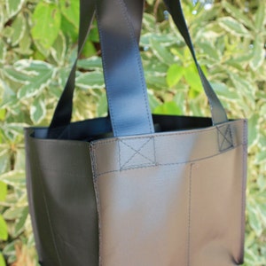 Könnte beinhalten: Eine schwarze wiederverwendbare Tragetasche mit zwei breiten Griffen. Die Tasche hat eine einzelne Tasche auf der Vorderseite.