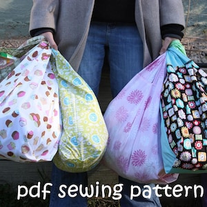 Op de afbeelding: Drie herbruikbare boodschappentassen met verschillende patronen. De tassen zijn gemaakt van stof en hebben een trekkoord. De patronen omvatten cupcakes, bloemen en klokken. De tassen worden vastgehouden door een persoon die een grijze jas en een blauwe spijkerbroek draagt. De tekst "pdf sewing pattern" staat onderaan de afbeelding.
