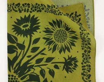 Może przedstawiać: Zielona bandana bawełniana z czarnym nadrukiem kwiatowym przedstawiającym słoneczniki i liście. Bandana ma obwódkę z małych czarnych kwiatów.