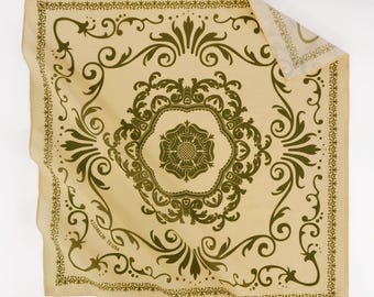 Könnte beinhalten: Ein quadratisches, beigefarbenes Bandana mit einem olivgrünen Blumen- und Scroll-Design. Die Mitte zeigt ein großes Blumenemblem, umgeben von verzierten Mustern. Die Ränder sind mit einem zarten Rand versehen. Der Text "#JJ24012B TX USA" ist unten links aufgedruckt.