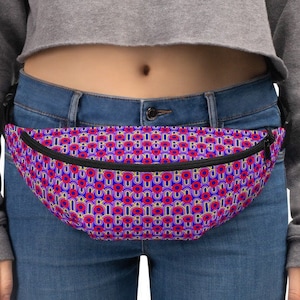 May include: A pink and blue fanny pack with a geometric pattern. The fanny pack is worn around the waist of a person wearing blue jeans.