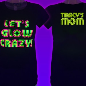Puede incluir: Dos camisetas negras con texto de ne&oacute;n. Una dice "LET'S GLOW CRAZY!" en verde, rosa y amarillo. La otra dice "TRACY'S MOM" en amarillo. Ambas camisetas tienen cuello redondo.