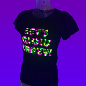 Puede incluir: Camiseta negra con el texto de ne&oacute;n "LET'S GLOW CRAZY!" en rosa, verde y amarillo. La camiseta se muestra en un maniqu&iacute; sobre un fondo p&uacute;rpura. El texto est&aacute; dise&ntilde;ado para brillar bajo luz negra.