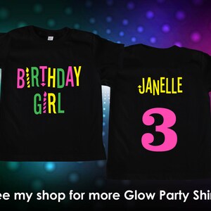 Puede incluir: Camisetas negras con texto y gr&aacute;ficos coloridos. Una camiseta dice "BIRTHDAY GIRL" en rosa, amarillo y verde con gr&aacute;ficos de velas. La otra camiseta tiene el nombre "Janelle" y el n&uacute;mero "3" en rosa.