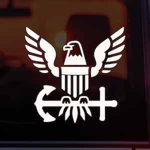 May include: White decal featuring a stylized eagle with outstretched wings, perched above an anchor and a sword. The eagle has a detailed head and is centered above a shield design. The design is suitable for vehicles or other surfaces.