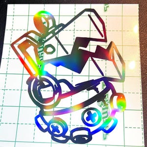 May include: Holographic sticker featuring a stylized figure in a wheelchair. The design uses black outlines with rainbow color gradients, creating a vibrant and eye-catching effect. The sticker is on a white background with a grid pattern.