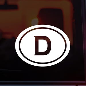 May include: White oval sticker with a black outline and the letter "D" in the center. The sticker is on a dark background.