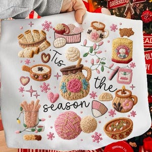 May include: White embroidered fabric with various baked goods and the phrase "Tis the season." The design includes pink and brown embroidered mugs, pastries, and decorative elements, perfect for holiday decor.