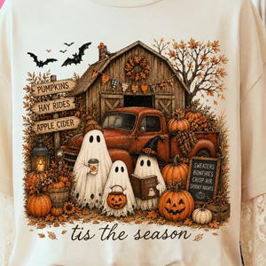 Può includere: Una t-shirt color crema con una grafica raffigurante un fienile rustico, un camion rosso e tre fantasmi. Il testo recita 'PUMPKINS', 'HAY RIDES', 'APPLE CIDER', 'SWEATERS', 'BONFIRES', 'CRISP AIR', 'SPOOKY NIGHTS' e 'tis the season'.