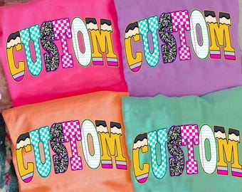 May include: Four brightly coloured t-shirts in pink, purple, orange, and teal. Each shirt displays the word "CUSTOM" in a school-themed design. The letters are outlined with pencils and filled with patterns.