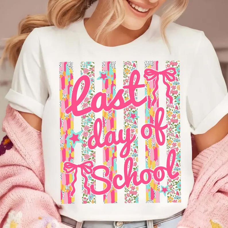 Puede incluir: Camiseta blanca con un dise&ntilde;o de rayas coloridas con estampados florales, estrellas y lazos. Las palabras "Last day of School" est&aacute;n escritas en rosa en la parte delantera. Se lleva una rebeca rosa sobre la camiseta.
