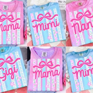 May include: Six pastel-colored t-shirts with text and bow designs. The shirts are pink, blue, and purple, each featuring a different name: "Mama", "Mimi", "Nana", and "Gigi". The design includes vertical stripes and star patterns.