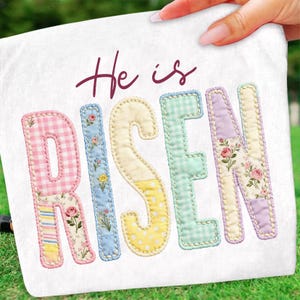 May include: A white decorative pillow with the words "He is Risen" in a script font and patchwork letters. The letters are in pastel colors and floral patterns, with a stitched border.