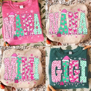 Puede incluir: Cuatro sudaderas en rosa, beige y verde, cada una con un nombre diferente en letras grandes y festivas. Los nombres son "MAMA", "NANA", "MIMI" y "GIGI", decorados con patrones rosas y verdes, gorros de Papá Noel y cajas de regalo.