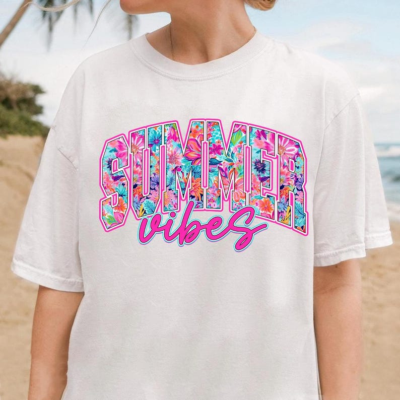 K&ouml;nnte beinhalten: Wei&szlig;es T-Shirt mit einem pink- und blaufarbenen Blumendesign, auf dem "Summer Vibes" steht.