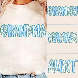 May include: A white t-shirt with blue and white striped letters that spell out "GRANDMA". The letters are decorated with a floral pattern. The image also shows three other shirts with the words "GRANNY", "MAMAW", and "AUNT" in the same style.