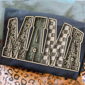 May include: Dark navy blue t-shirt with the word "MAMA" in a varsity-style font. The letters feature a camouflage, checkered, and distressed design with a tan outline.
