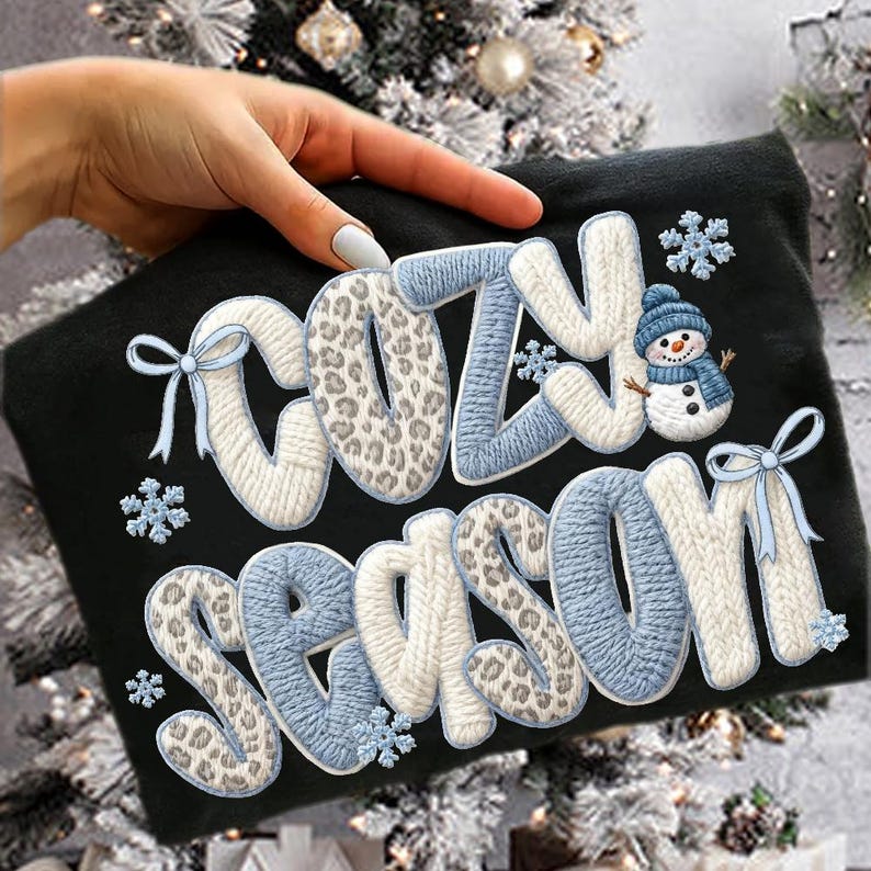 Pu&ograve; includere: T-shirt nero con le parole "COZY SEASON" in stile lavorato a maglia, con accenti blu e bianchi, dettagli animalier, fiocchi di neve e una grafica a pupazzo di neve. Un design festivo a tema invernale.