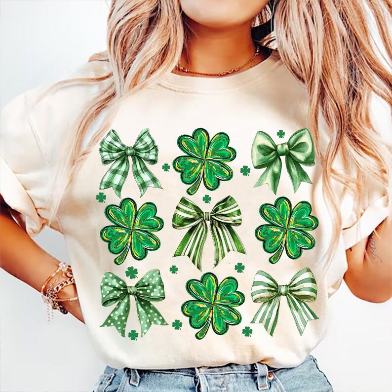May include: A white t-shirt featuring a green shamrock and bow design. The shamrocks are four-leaf clovers and the bows are in various green patterns.