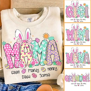 May include: A beige sweatshirt with a colorful Easter-themed design that says "MAMA" with bunny ears and a bow. The design also includes a sun, flowers, and eggs. The names Gavin, Mandy, David, Henry, and Sophia are printed below the design.