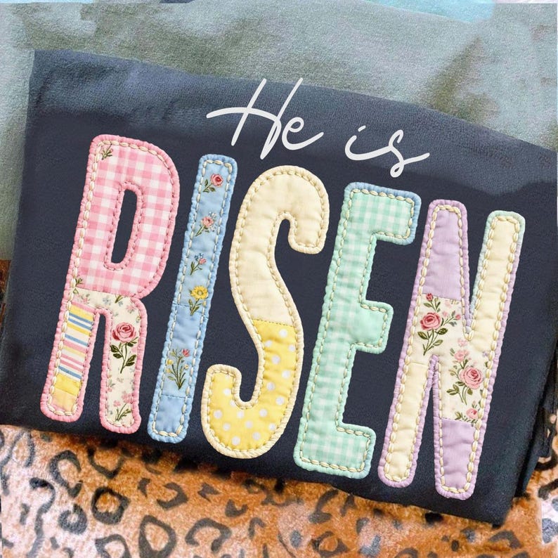 May include: A dark gray t-shirt with the words "He is Risen" in a patchwork design. The letters are in pastel colors with floral and gingham patterns. The overall theme is Easter.