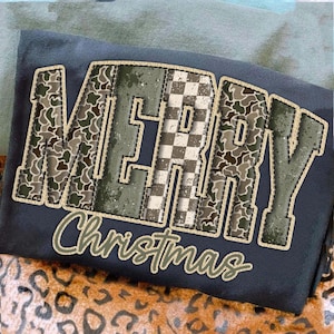 Può includere: Una felpa blu navy con la scritta "MERRY Christmas" in un design cucito e invecchiato. Le lettere hanno un motivo mimetico e a scacchi, con un contorno beige. Il testo "Christmas" è in corsivo.