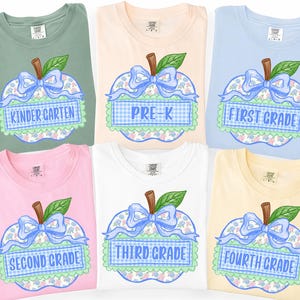Op de afbeelding: Zes t-shirts met korte mouwen in saliegroen, perzik, lichtblauw, roze, wit en geel. Elk shirt heeft een appelafbeelding met een blauwe strik, groen blad en een blauw geblokte banner met de tekst KINDER GARTEN, PRE-K, FIRST GRADE, SECOND GRADE, THIRD GRADE of FOURTH GRADE.