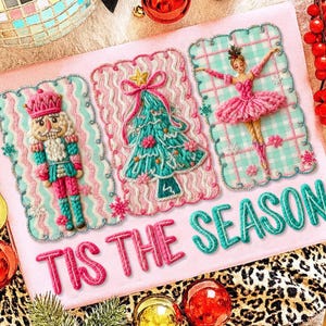 May include: A pink Christmas card with embroidered designs of a nutcracker, Christmas tree, and ballerina. The card has the text "TIS THE SEASON" in pink and teal. Ornaments and a leopard print pattern are in the background.