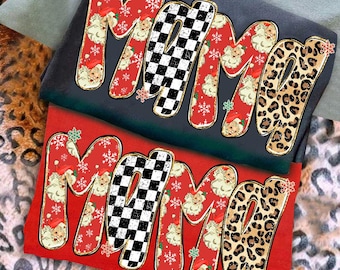 May include: Two t-shirts with the word "MAMA" in a festive design. The letters feature a mix of patterns, including Santa Claus, snowflakes, a black and white checkerboard, and leopard print. One shirt is red, the other is dark grey.