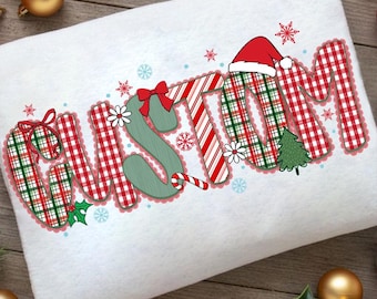 May include: A white Christmas-themed towel with the word "CUSTOM" in a festive design. The letters are filled with red and green plaid, candy cane stripes, and a Santa hat. Snowflakes, bows, and a small Christmas tree add to the holiday theme.