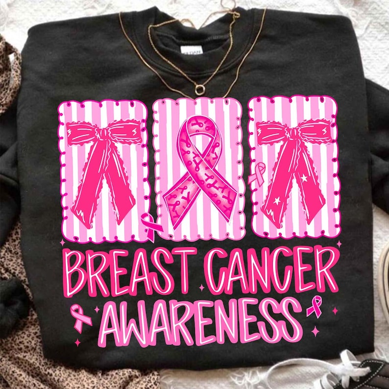May include: Black sweatshirt with a pink and white striped design featuring pink bows and a pink ribbon. The words "BREAST CANCER AWARENESS" are printed in pink script below the design.