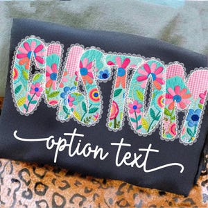 May include: Dark gray sweatshirt with the word "CUSTOM" in a floral design with a white lace trim. The text "option text" is written in a cursive font below the word "CUSTOM".