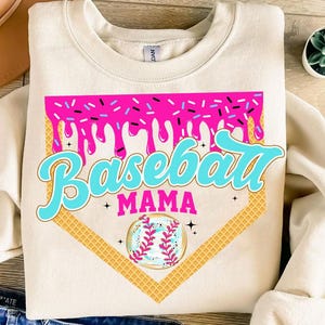 May include: A white sweatshirt with a pink and blue baseball graphic. The graphic features a baseball diamond, a baseball, and the text "Baseball Mama".