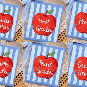 May include: Six square, light blue and white striped gift boxes with a red apple graphic and grade level text. The grades include Kindergarten, First Grade, Pre-K, Fourth Grade, Third Grade, and Second Grade.