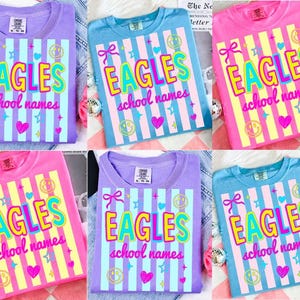 Puede incluir: Una colecci&oacute;n de seis camisetas en varios colores, incluyendo morado, azul y rosa. Cada camiseta presenta la palabra "EAGLES" en una fuente colorida y audaz, junto con "school names" y elementos decorativos como corazones y estrellas.