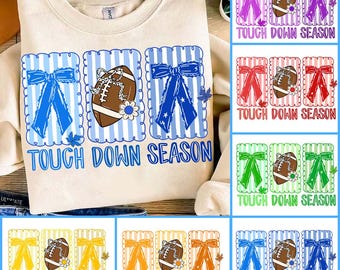 May include: A cream-coloured sweatshirt with a football-themed graphic. The design includes a football, bows, and the text "TOUCH DOWN SEASON" in blue. Additional colour variations of the design are also shown.