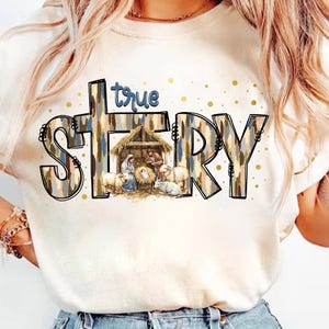 May include: White t-shirt with a brown and blue patterned design that says "true story" with a nativity scene in the middle of the word "story".