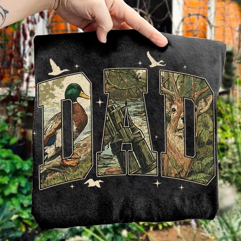 K&ouml;nnte beinhalten: Schwarzes T-Shirt mit dem Wort "DAD" in einem Design zum Thema Natur. Die Buchstaben sind mit Bildern einer Ente, eines Fernglases und eines Hirsches gef&uuml;llt. Wei&szlig;e V&ouml;gel und Sterne sind ebenfalls abgebildet.