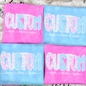 May include: Four custom t-shirts in pink and blue. Each shirt features the word "CUSTOM" in a floral and polka dot design with a scalloped edge. Below the word is the names "Layla, Oliver, Taylor".