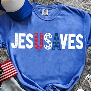May include: Blue t-shirt with the text "JESUS SAVES" in white block letters. The letter "U" is red with white stars, and the letter "S" is blue with white stars. A blue and white trucker hat and an American flag are also visible.