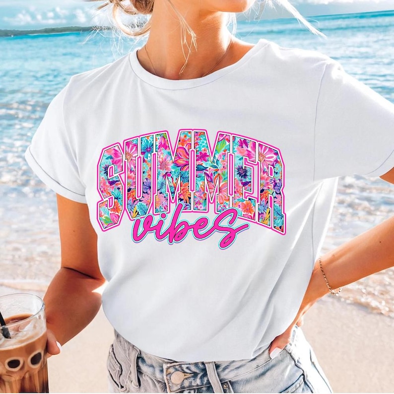 K&ouml;nnte beinhalten: Wei&szlig;es T-Shirt mit einem floralen Druckdesign, auf dem "SUMMER vibes" in rosa Buchstaben steht.
