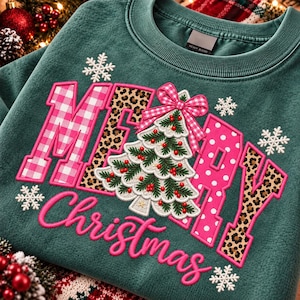 May include: A dark green crewneck sweatshirt featuring the word MERRY in large block letters with pink gingham, leopard print, and white polka dot patterns. A Christmas tree with red berries and a pink gingham bow sits in the center, with the word Christmas below.