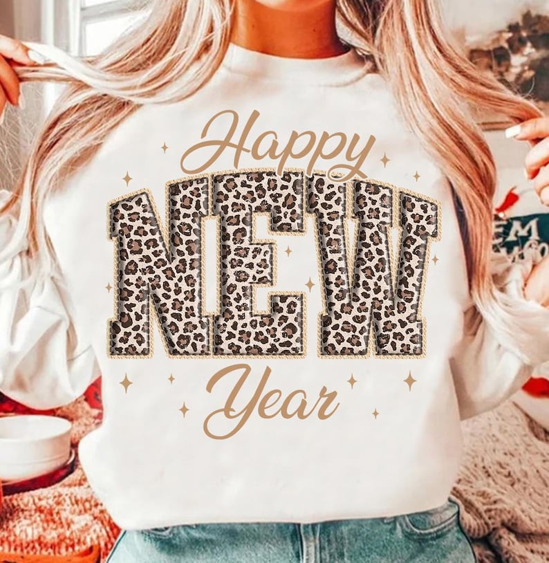 K&ouml;nnte beinhalten: Wei&szlig;es Sweatshirt mit dem Schriftzug "Happy NEW Year" in goldener Schrift und Leopardenmuster-Blockbuchstaben. Das Design enth&auml;lt goldene Sternakzente. Ein festliches Oberteil zum Feiern des neuen Jahres.