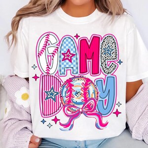 May include: White t-shirt with a pink, blue, and white graphic that says "GAME DAY" with a baseball and a bow.