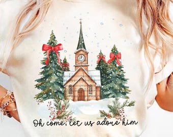 May include: A white t-shirt with a watercolor illustration of a church with snow falling. The church has a steeple and a clock tower. There are two pine trees with red bows on either side of the church. The text "Oh come, let us adore him" is printed below the illustration.