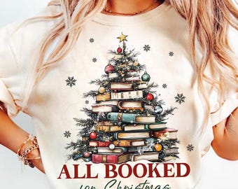 May include: A white t-shirt with a Christmas tree made of books and the text "All Booked for Christmas".