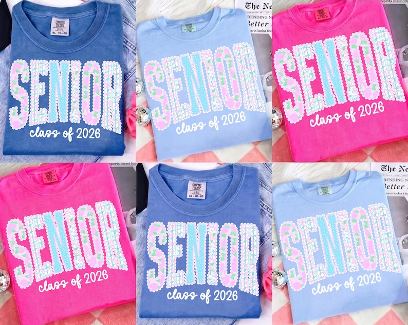 May include: A collection of six t-shirts in various colors: blue, light blue, and pink. Each shirt features the word "SENIOR" in large, sequined letters, with "class of 2026" below. The shirts are casual and likely for graduation.