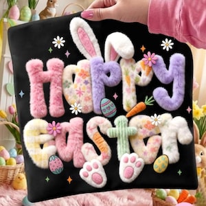 Op de afbeelding: Zwart kussen met de woorden "Happy Easter" in zachte, pastelkleurige letters. Het ontwerp bevat konijnenoren, wortels, paaseieren, bloemen en pootafdrukken. Het kussen is versierd met glinsterende sterren en madeliefjes.
