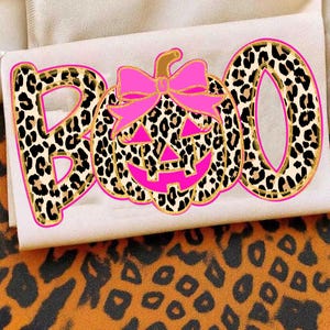 May include: A graphic design featuring the word BOO with a leopard print pattern and a bright pink outline. The letter O is replaced by a pumpkin with a leopard print texture, a bright pink bow, and a carved face with bright pink accents.